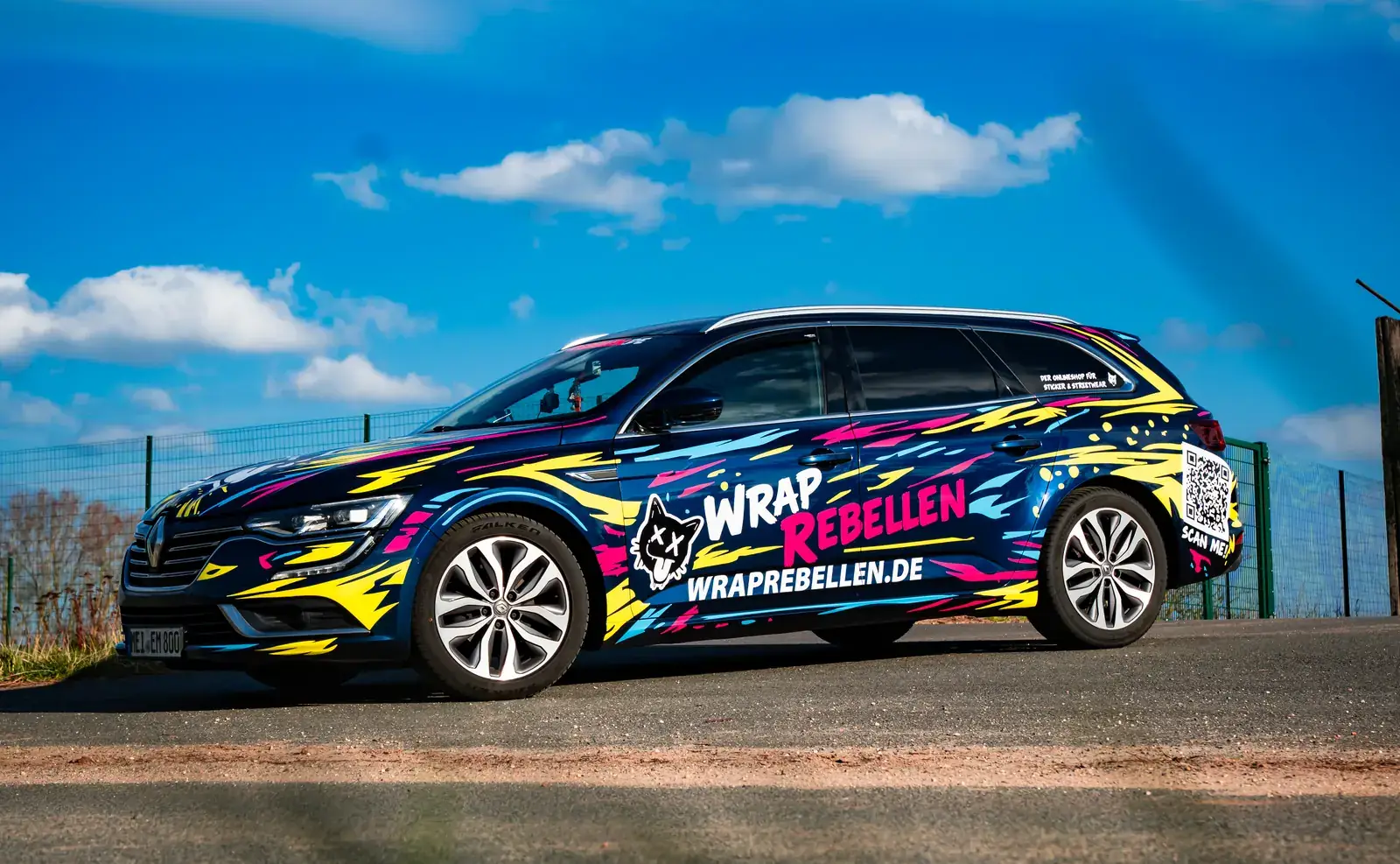 Firmenwagen von Wrap Rebellen mit auffälliger Folierung, Katzenlogo und Webadresse vor blauem Himmel